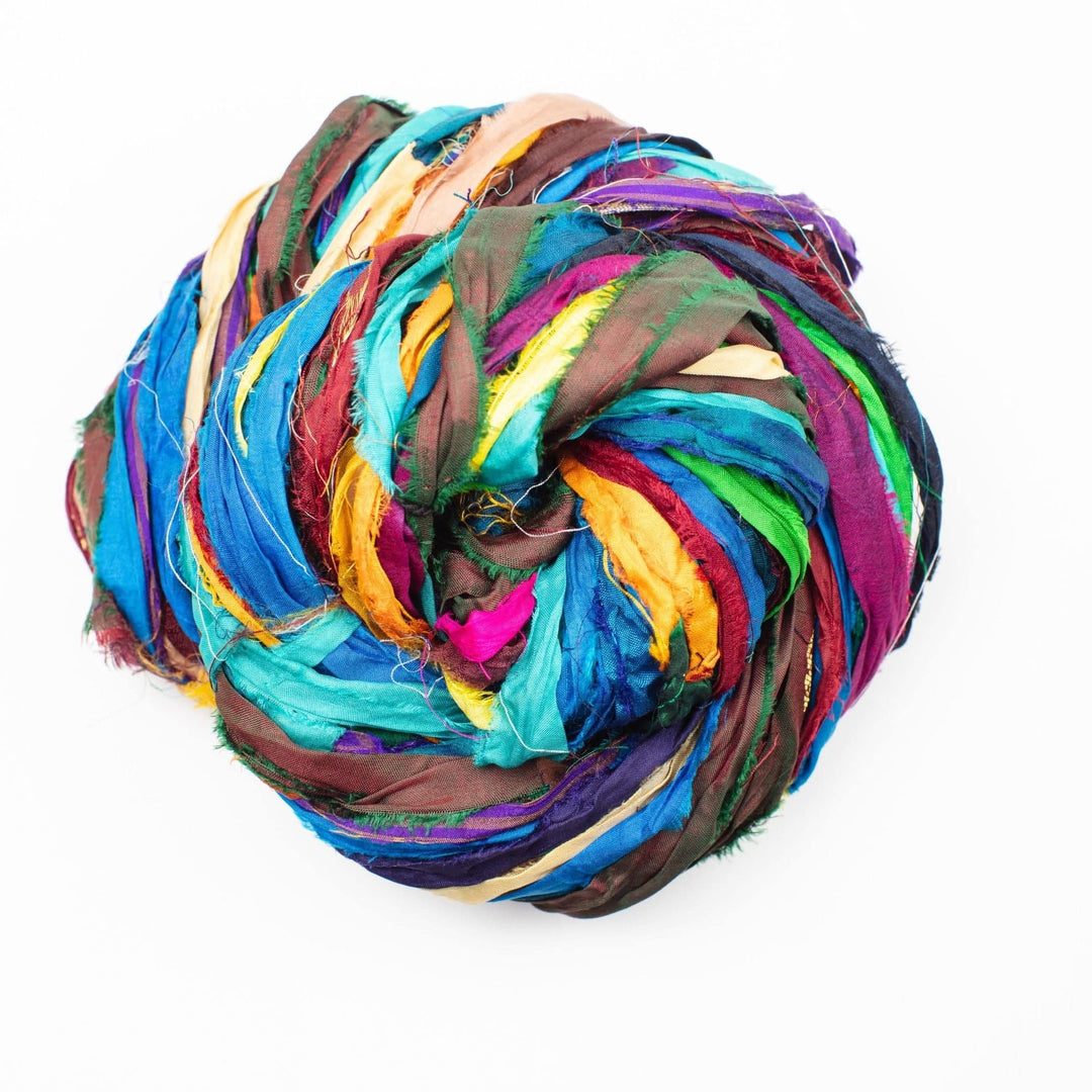 A ball of colorful yarn made from various strips of fabric in shades of blue, green, yellow, pink, and brown, tightly wound together.