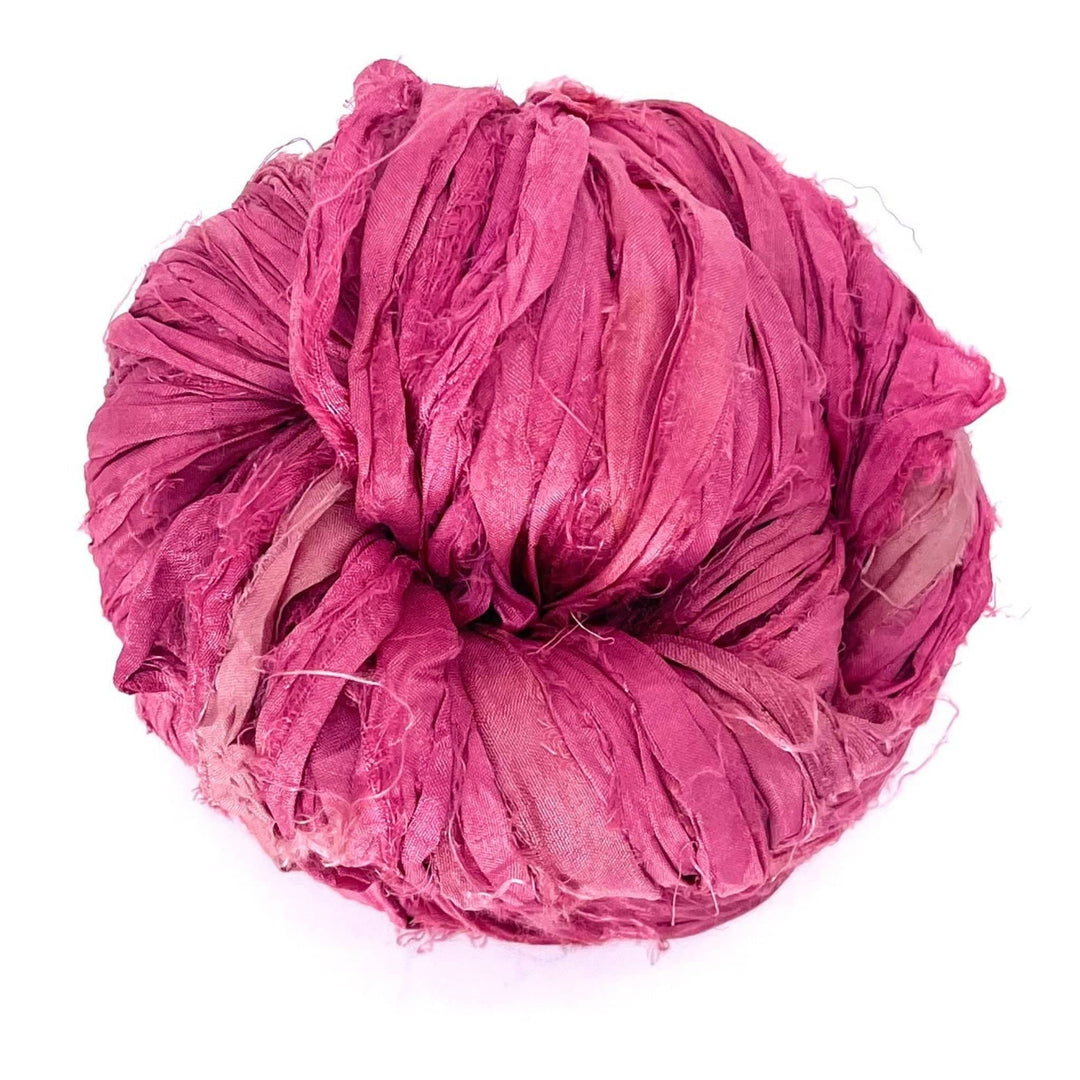 A large ball of pink ribbon yarn, tightly wound in uniform layers.