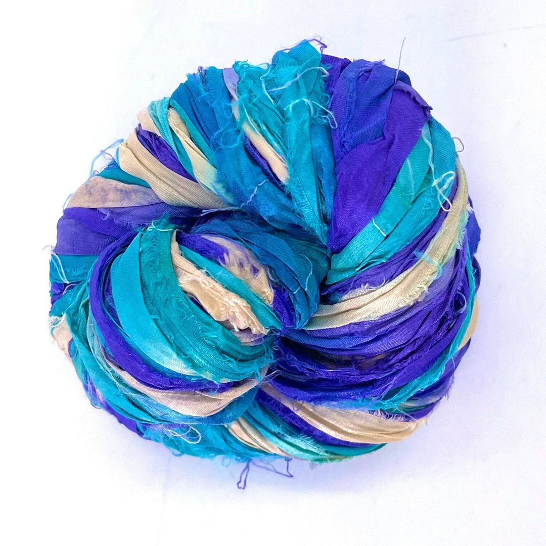 Ball of multicolored yarn in blue, purple, and beige, loosely wrapped against a white background.