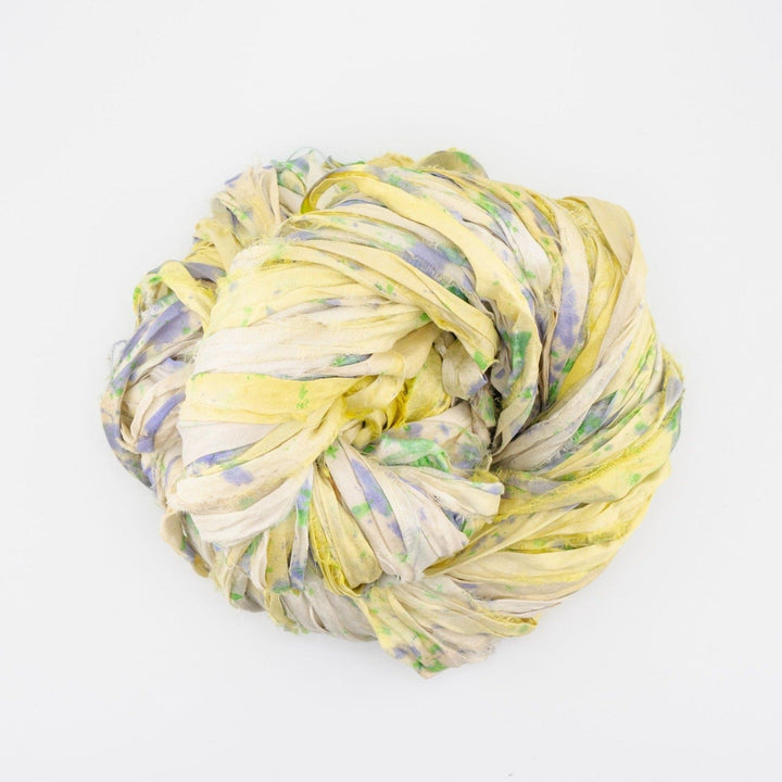 Coiled bundle of multicolored silk ribbon in yellow, green, and purple on a white background.