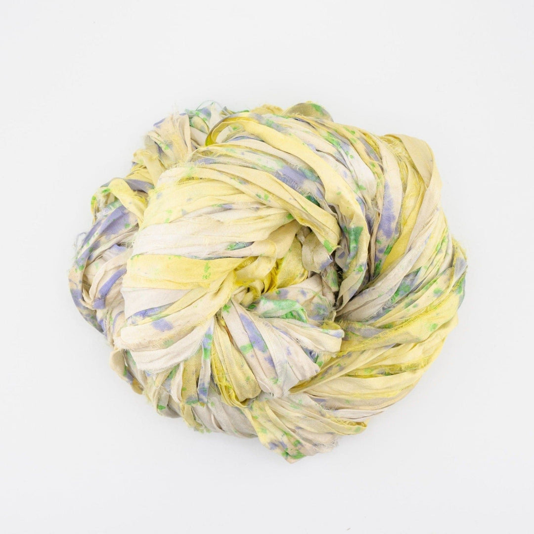 Coiled bundle of multicolored silk ribbon in yellow, green, and purple on a white background.